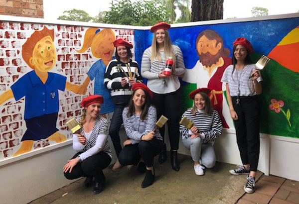 Teachers paint the school Our Lady of Mt Carmel Catholic Primary School Mt Pritchard teachers stand in front of their school art mural.