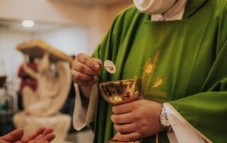 Priest presenting the Consecrated host to a parishioner in COVID times
