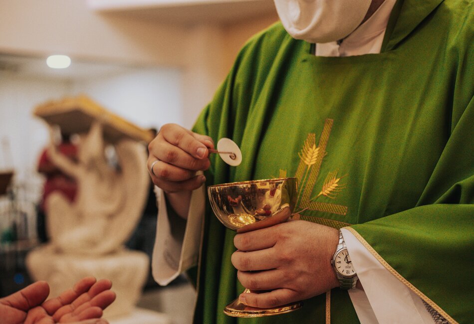 Priest presenting the Consecrated host to a parishioner in COVID times