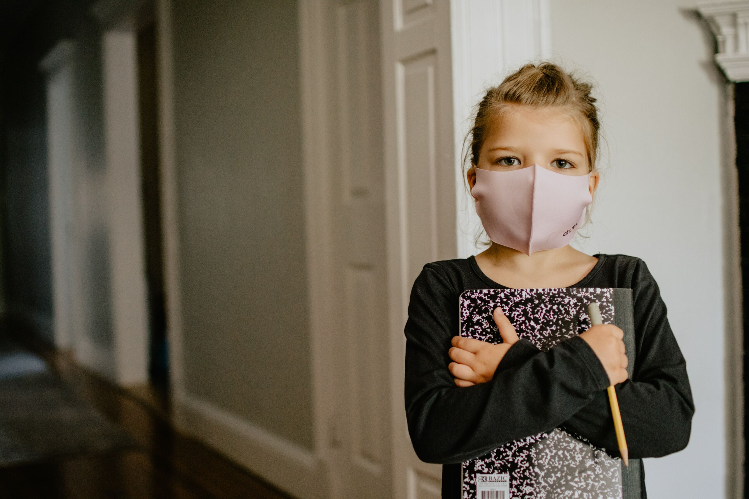 A girl wearing a COVID mask holding a book