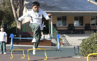Boy jumping over hurdles in school playground at St Pter Chanel Catholci primary School Regents Park.