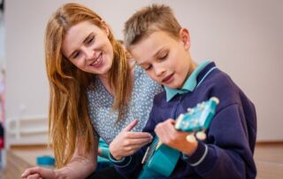 A student learns guitar with his music teacher.