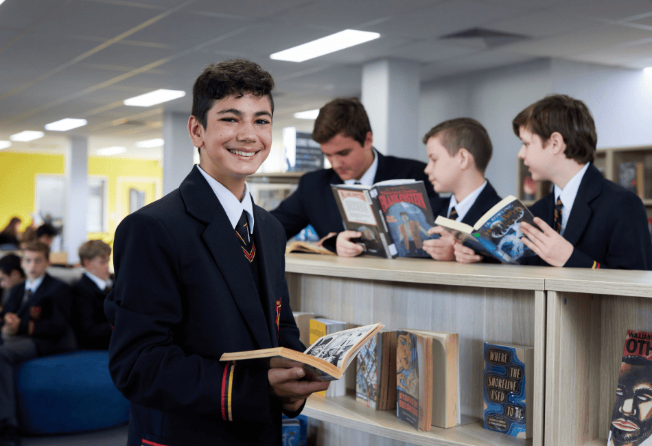 Secondary school student smiling with a book while his three friends in the background also read A photo of a secondary school student smiling with a book while his three friends in the background also read
