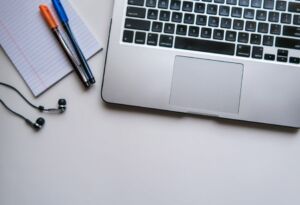 Laptop, pens, notepad and ear buds on a desk - Photo by Maya Maceka on Unsplash