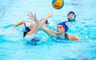 Female athletes reach for the ball in Sydney Catholic Schools' 2022 Water Polo Championships at Ashfield Aquatic Centre