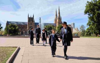 St Mary's Cathedral students, boys and girls of various ages, walk in Hyde Park with the beautiful St Mary's Cathedral as the backdrop.