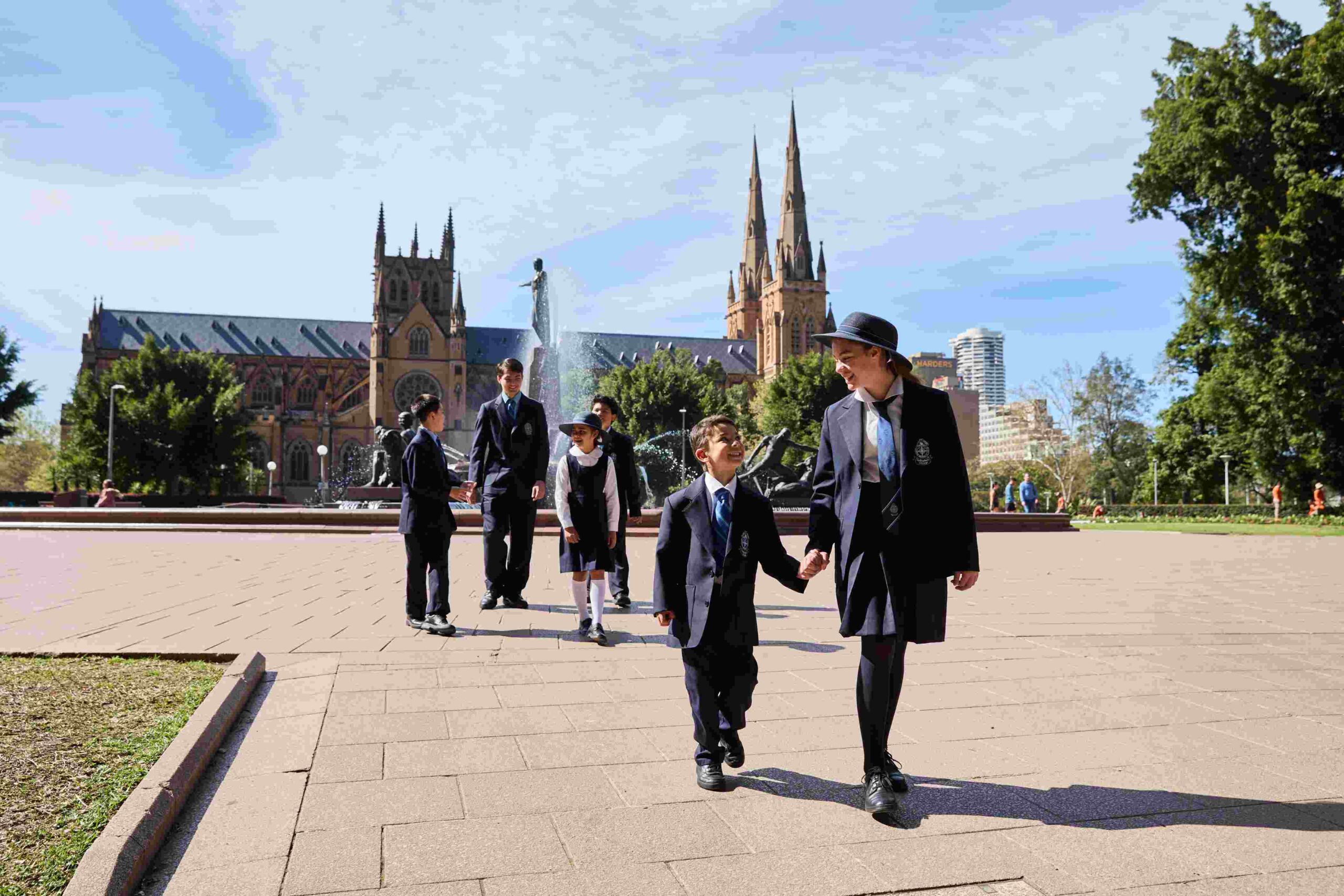 St Mary's Cathedral students, boys and girls of various ages, walk in Hyde Park with the beautiful St Mary's Cathedral as the backdrop.
