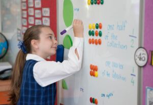 A Kindergarten student completes a mathematics activity on a school whiteboard.